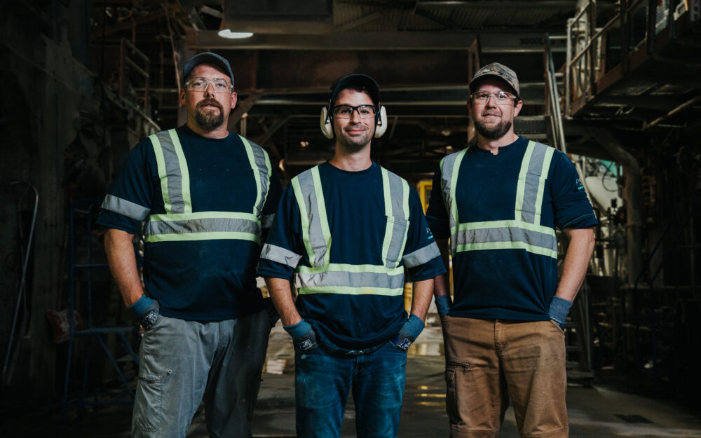 Paper mill employees pose in front of machinery